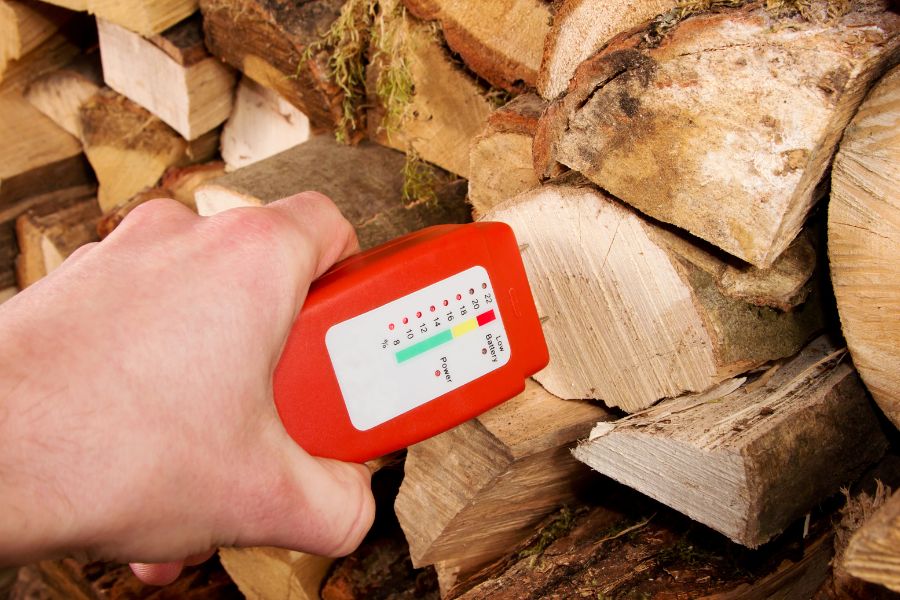 Hand with a wood moisture meter in front of a stack of wood