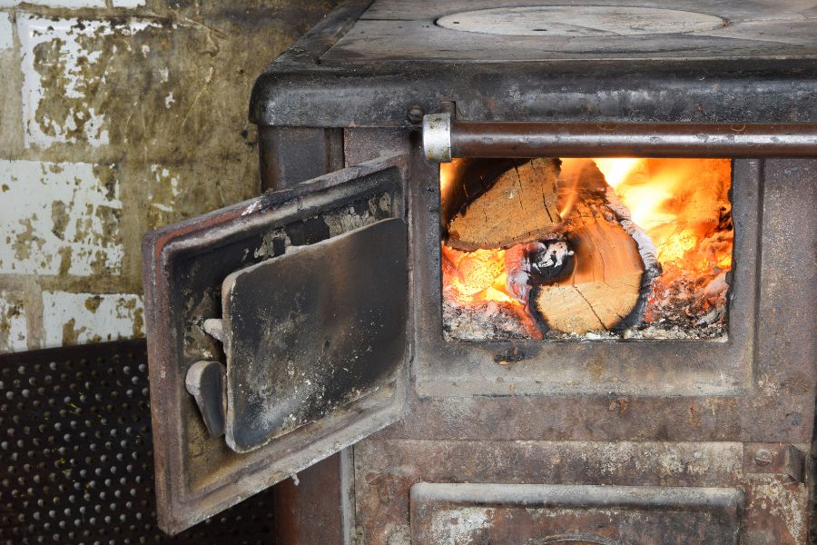 A burning wood stove with old and damaged looking