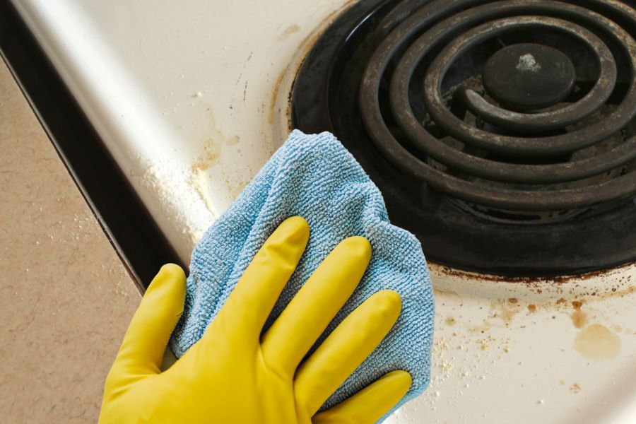Hand with cleaning glove wiping off extra food on coil stovetop
