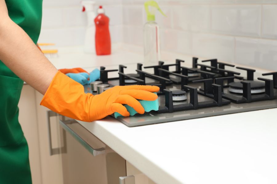 Woman cleaning gas stove with sponge in the kitchen