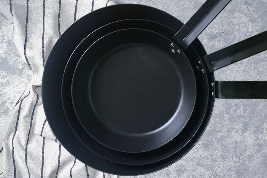 Set of carbon steel pan on grey surface with kitchen napkin
